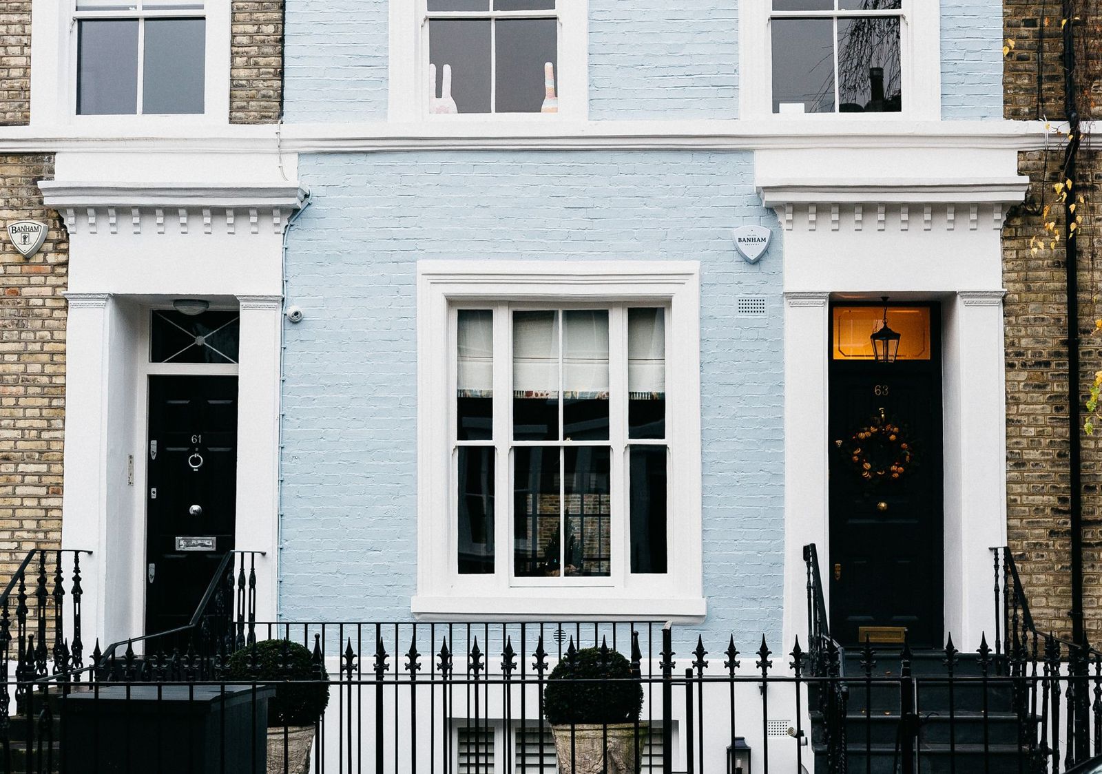 A pale blue painted row house with white trim and black front doors, fronted by a black ornamental metal fence with spear-point pickets and handrails.